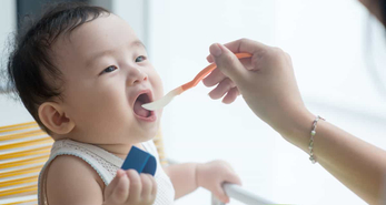 After seeing the signs baby is ready for solid food, a parent introduces very amounts on a baby spoon as part of the baby weaning process.