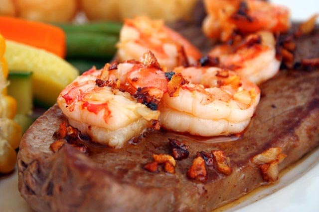 close up of shrimp on steak and vegetables in the background