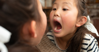 Young child checking in the mirror to see if her milk tooth has fallen out.