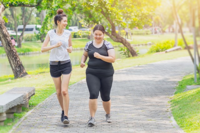 Two women encouraging each other while jogging in the park.