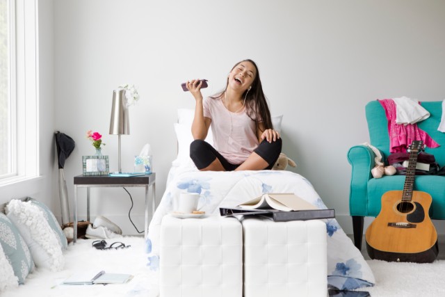 teenager in her room full of hobby items sitting on bed