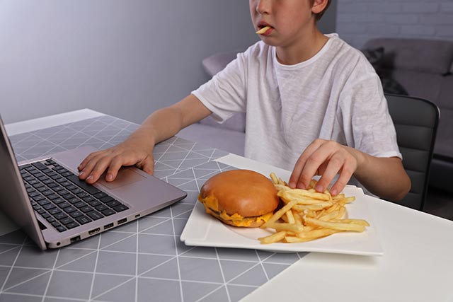 Teenager eating burget and fries while playing the computer