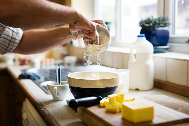 A man adding baking ingredients into a bowl