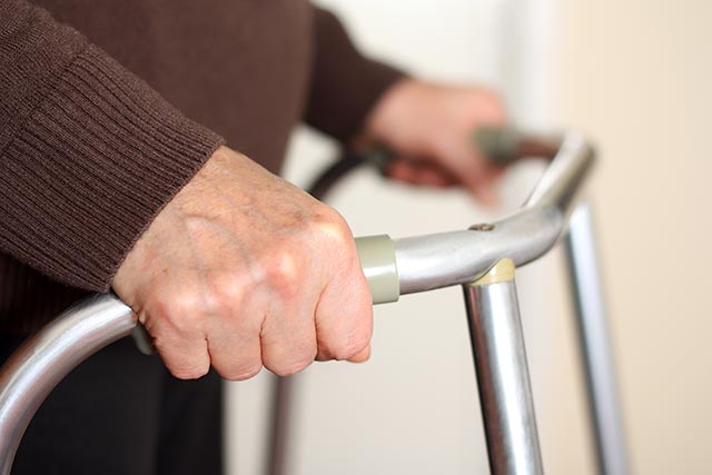 Elderly lady gripping the handles of her walking frame