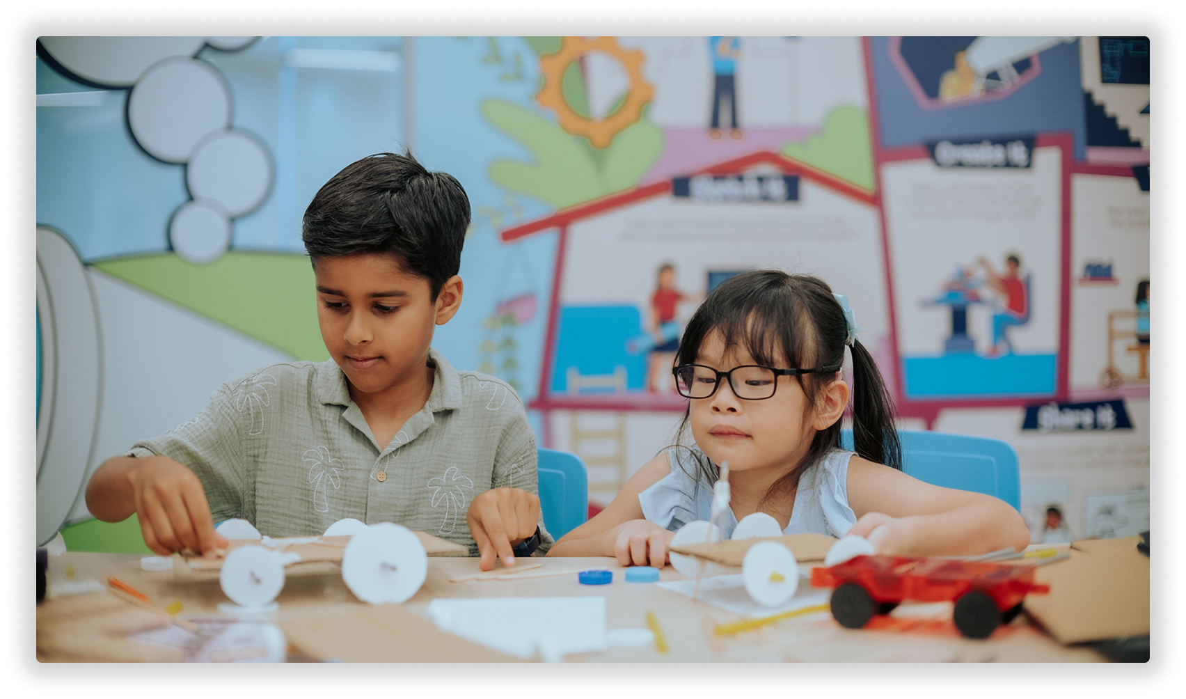 Children creating a model car with craft materials in a classroom.