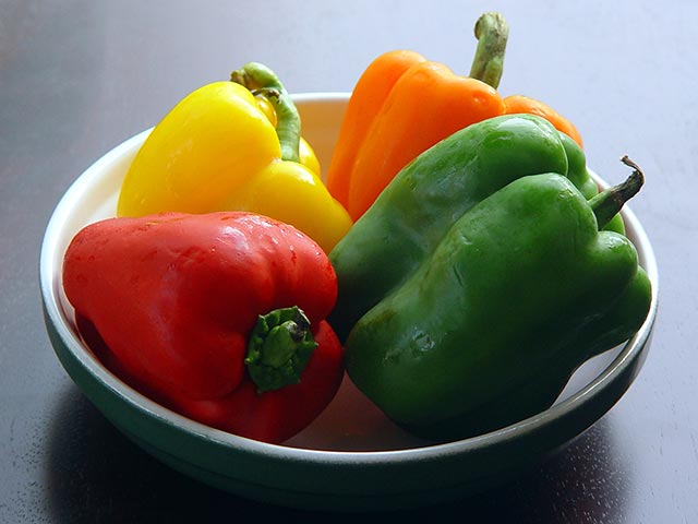 red, yellow orange and green peppers in a bowl