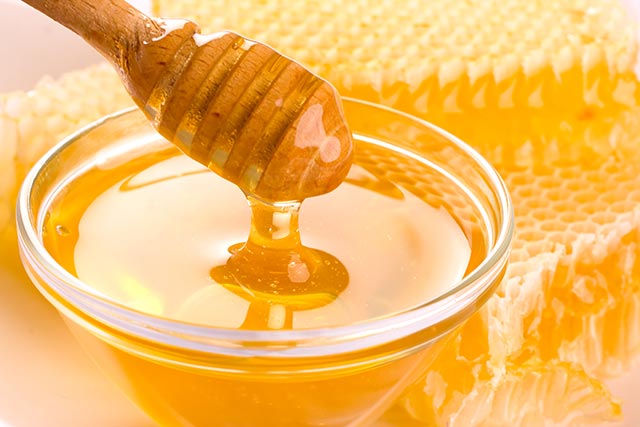 A wooden spoon dipped into a bowl of honey, surrounded with honeycombs